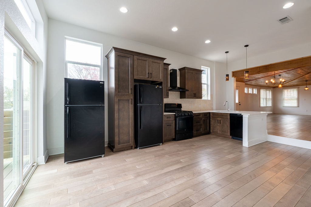 2016 Peoples Street Austin, TX 78702 - Photo 6 of 28 Kitchen with black appliances, light countertops, dark brown cabinets, wall chimney exhaust hood, and hanging light fixtures