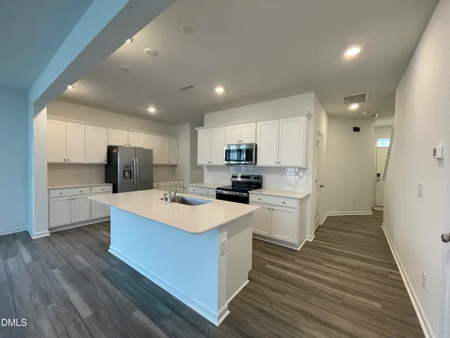 a large white kitchen with wooden floor and stainless steel appliances