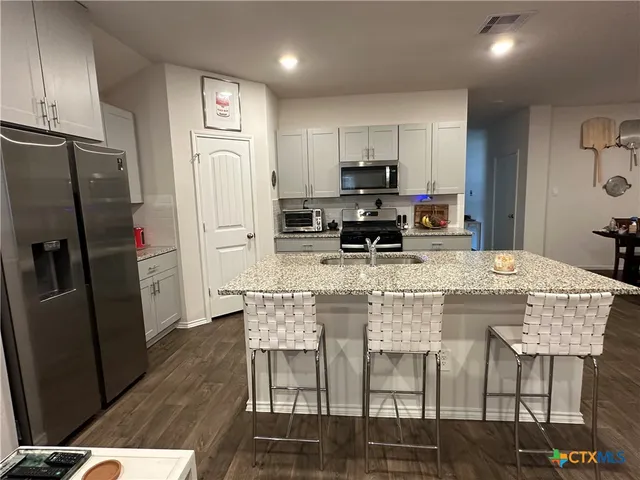 a kitchen with stainless steel appliances kitchen island granite countertop a refrigerator a stove a microwave oven a sink with island and chairs