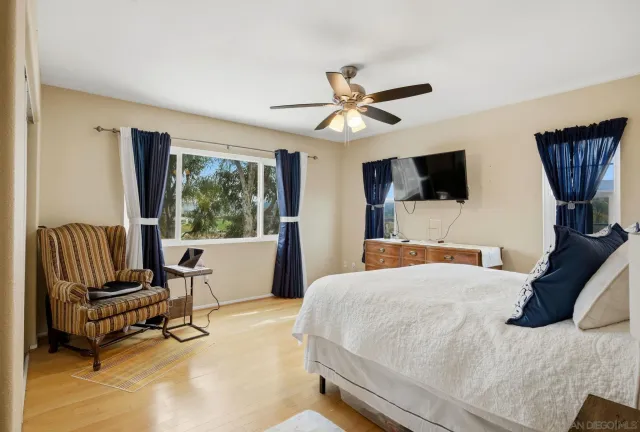 a bedroom with a bed a chair a computers on the table and a large window