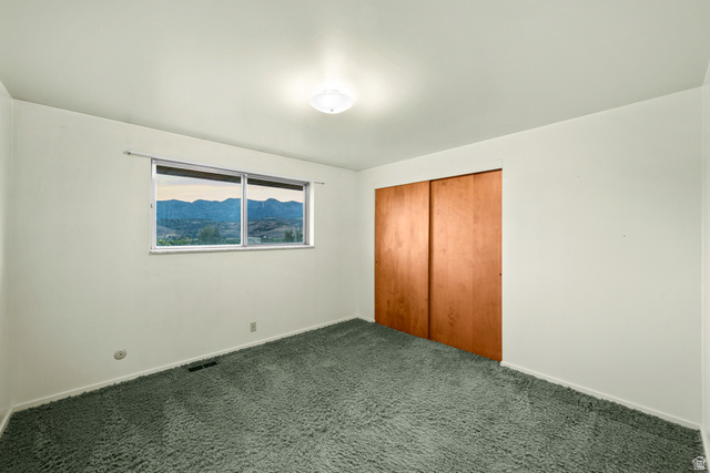 1940 West Old Hwy Road Morgan, UT 84050 - Photo 37 of 73 Interior room featuring a large window with distant mountain scenery, plush green carpeting, neutral wall finishes, a ceiling-mounted light fixture, and a spacious closet with wood panel doors