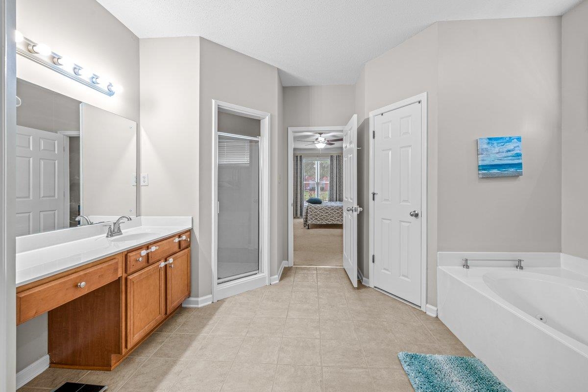 4840 Rainy Pass Road Collierville, TN 38017 - Photo 24 of 30 Spacious bathroom featuring a double vanity with wood-finish cabinetry, a large frameless mirror, a glass-enclosed shower, and a white soaking tub