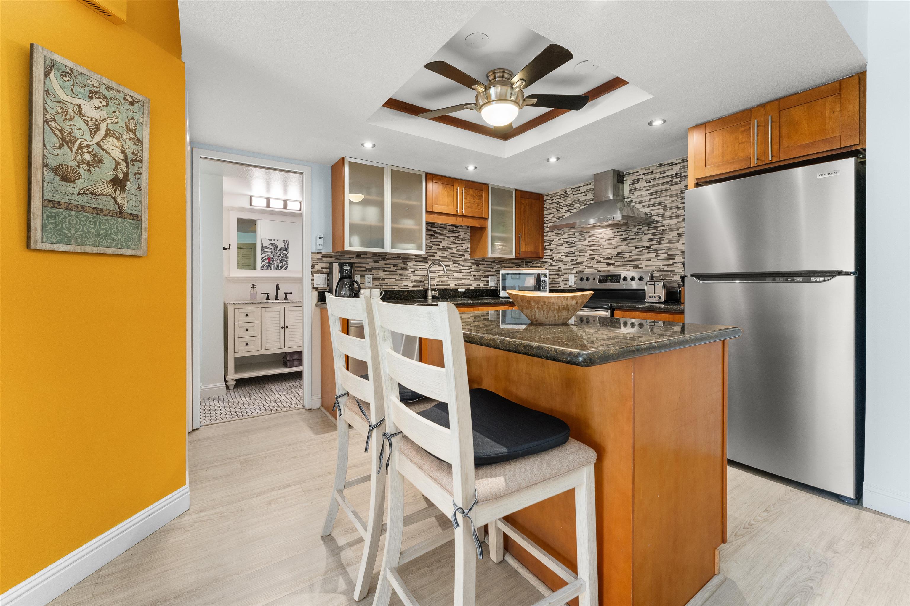 2575 South Kihei Road, Unit T110 Kihei, HI 96753 - Photo 12 of 24 a kitchen with stainless steel appliances granite countertop a refrigerator a stove a sink a dining table and chairs with wooden floor