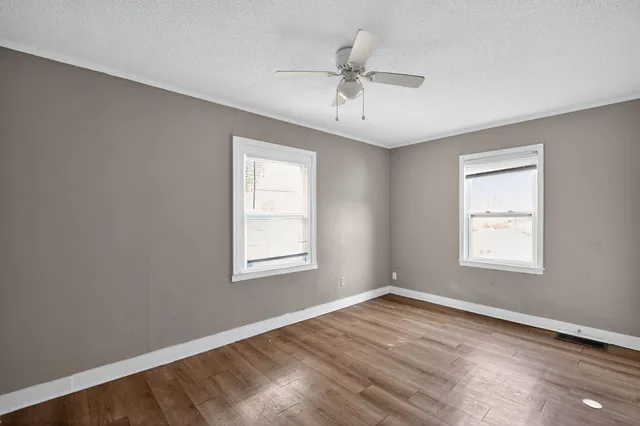 an empty room with wooden floor fan and windows