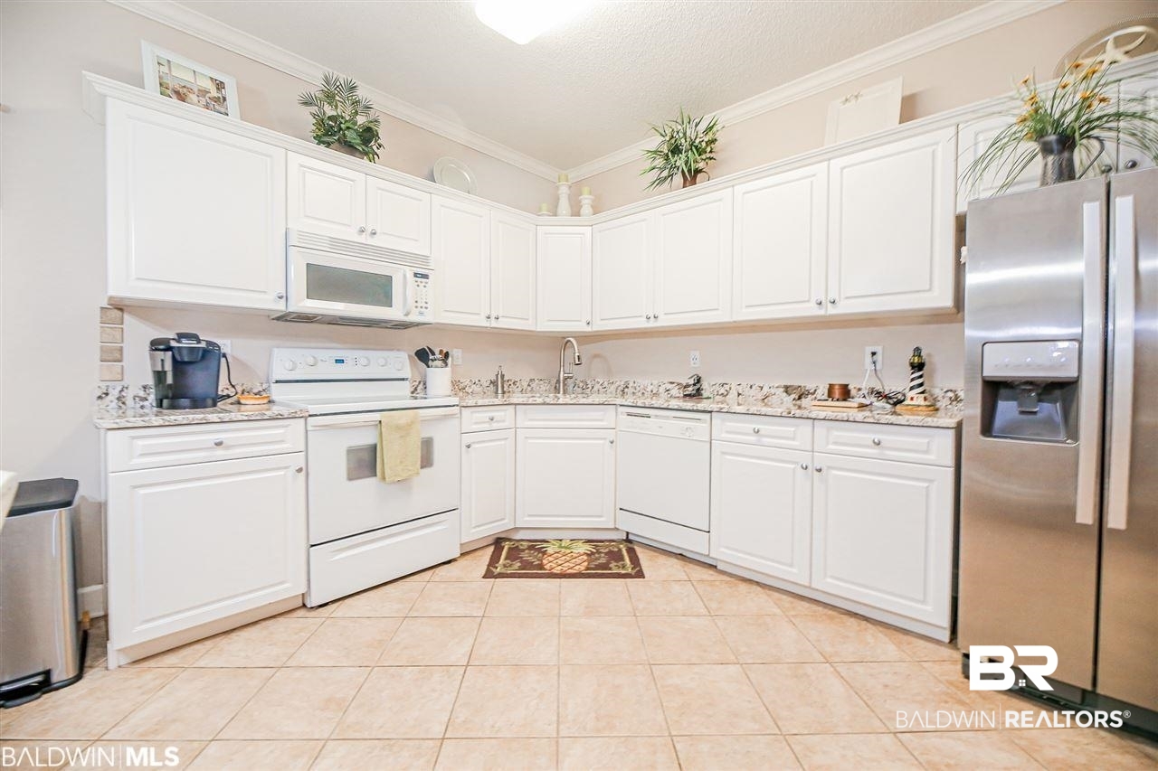 Kitchen with white cabinets, ornamental molding, light tile patterned flooring, light stone counters, and white appliances