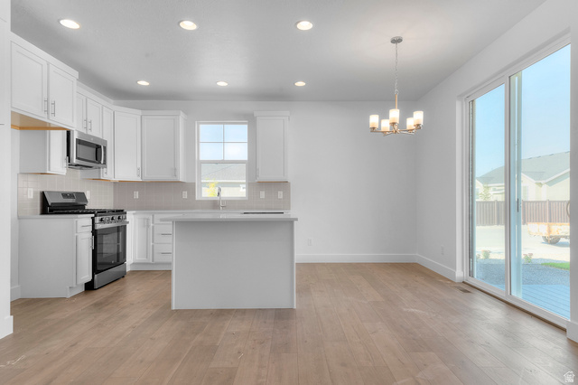5644 Ibis Road Tooele, UT 84074 - Photo 14 of 19 Open-concept kitchen featuring white shaker cabinetry, stainless steel appliances, a center island with countertop seating, and wood-finish flooring