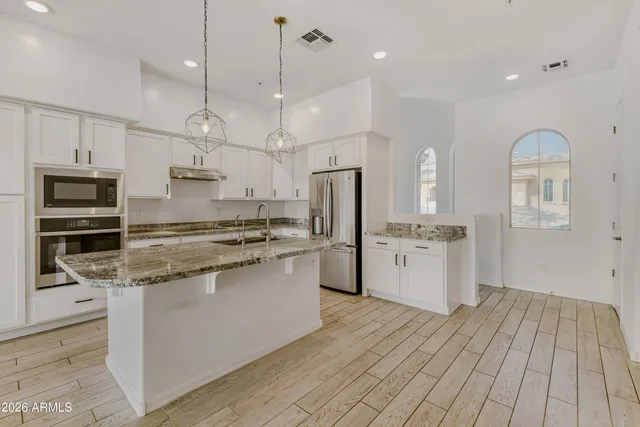 a kitchen with stainless steel appliances kitchen island granite countertop a refrigerator a stove and white cabinets with wooden floor