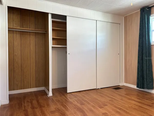 a view of an empty room with wooden floor and closet area