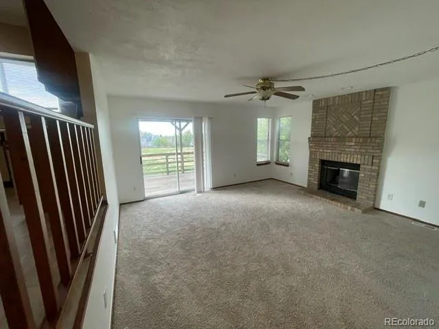 an empty room with windows fireplace and a ceiling fan