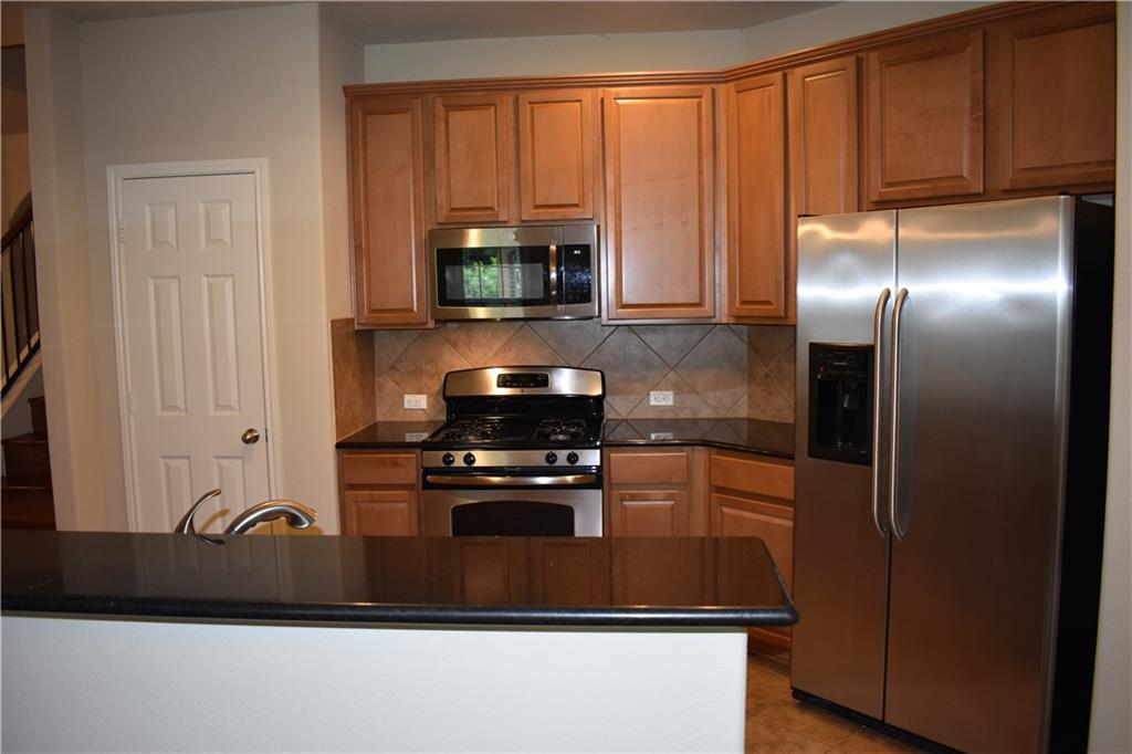 1310 West Parmer Lane, Unit 1503 Austin, TX 78727 - Photo 3 of 26 Kitchen featuring stainless steel appliances, dark stone counters, tasteful backsplash, and wood finish cabinets