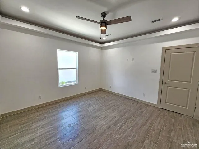 an empty room with wooden floor ceiling fan and windows