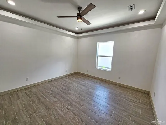 an empty room with wooden floor ceiling fan and windows