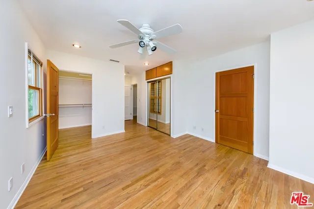 a view of an empty room with wooden floor and a ceiling fan
