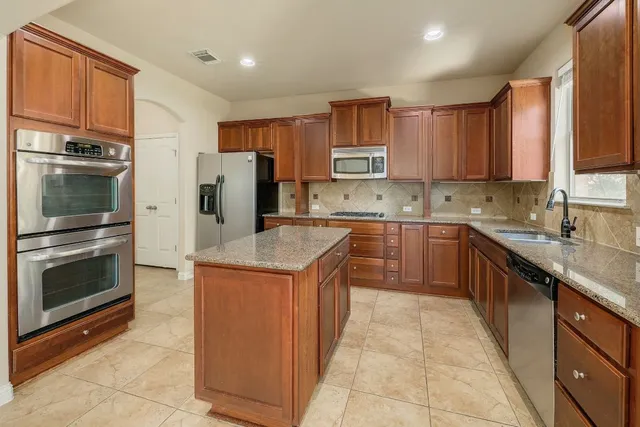 a kitchen with stainless steel appliances granite countertop a stove top oven a sink dishwasher a refrigerator and a microwave oven with large wooden cabinets