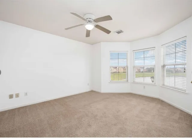 an empty room with chandelier fan and windows
