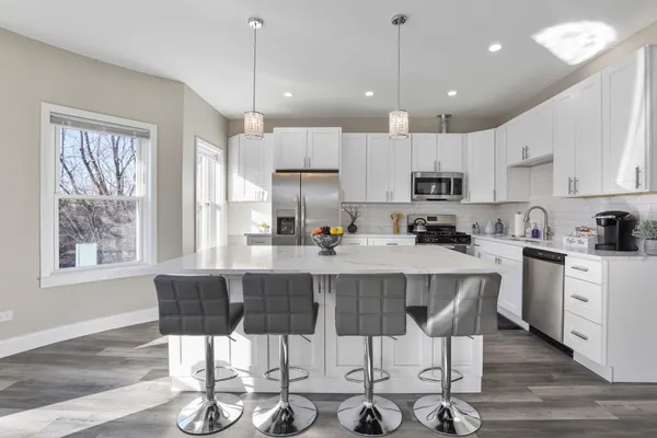 a kitchen with stainless steel appliances kitchen island granite countertop a dining table chairs and white cabinets