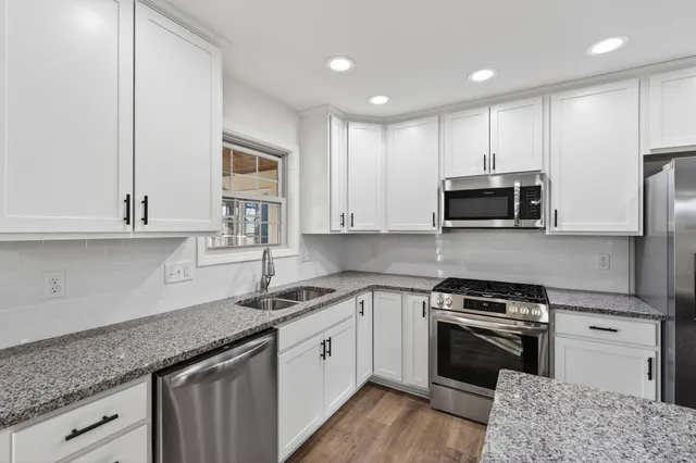 a kitchen with granite countertop white cabinets stainless steel appliances and a wooden floor