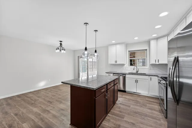 a kitchen with stainless steel appliances granite countertop a sink a stove a refrigerator and island with wooden floor