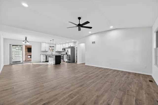 an empty room with a kitchen and a ceiling fan wooden floor