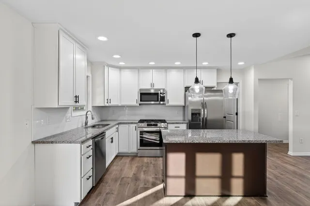 a large kitchen with granite countertop a stove a sink a center island and stainless steel appliances