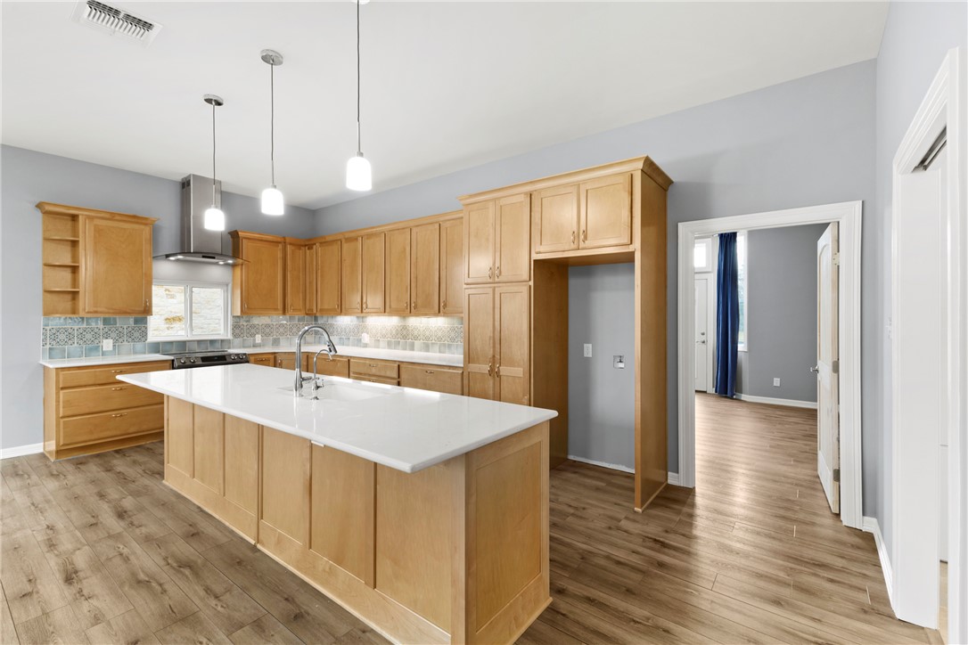 504 North Street Columbus, TX 78934 - Photo 5 of 29 Kitchen with wall chimney range hood, a center island with sink, light brown cabinetry, and decorative light fixtures