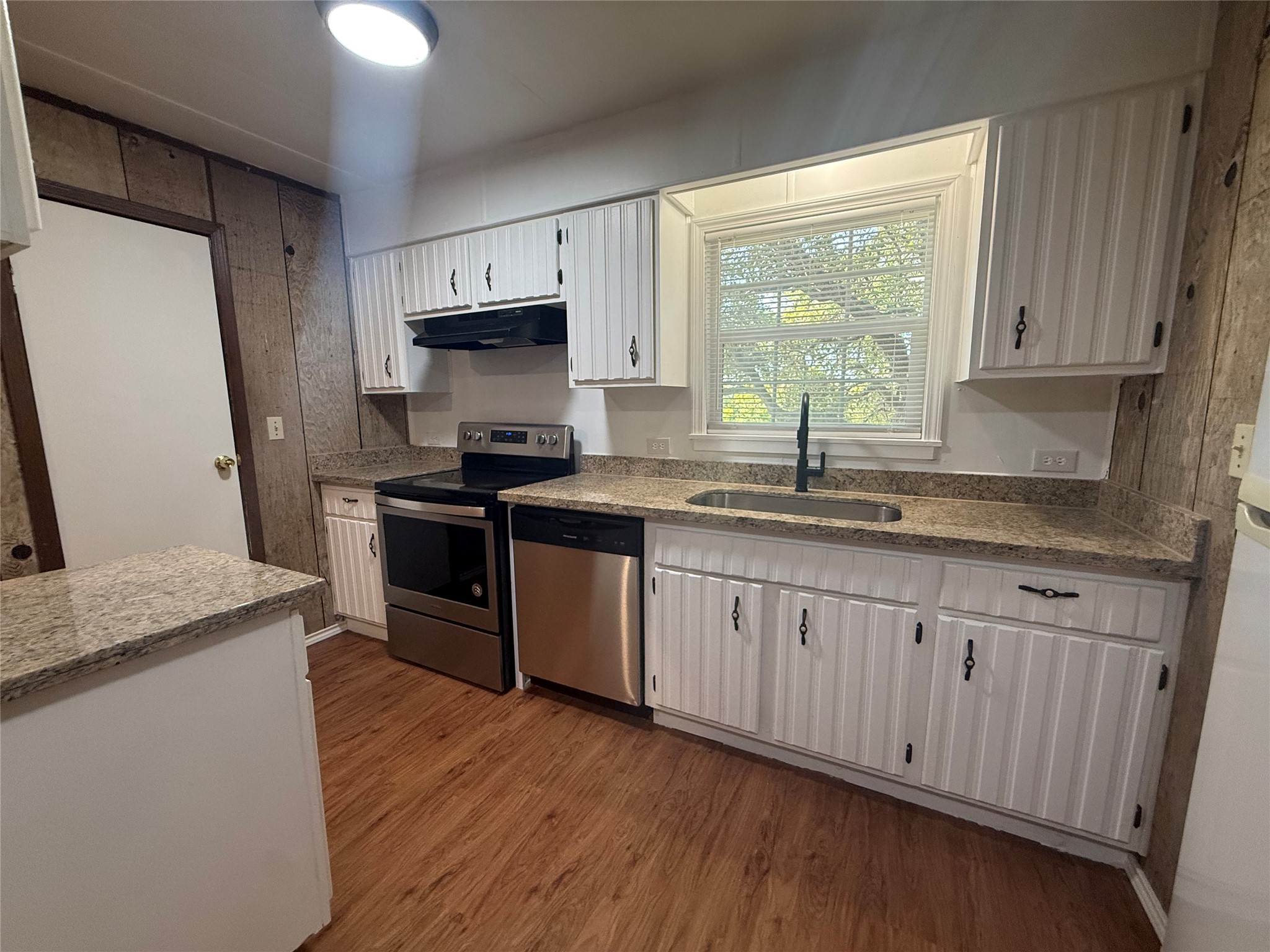 23393 Nameless Road, Unit 112 Leander, TX 78641 - Photo 9 of 16 White beadboard cabinetry pairs with stone-patterned countertops and rich wood-toned flooring in this classic kitchen.