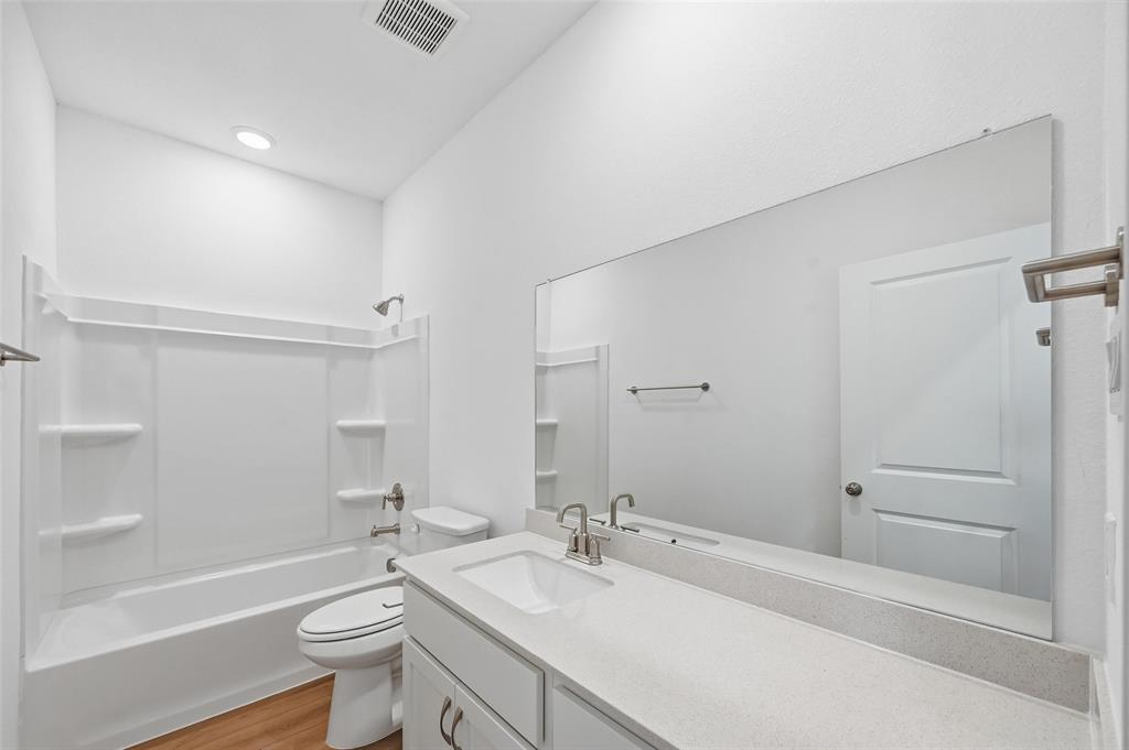1168 Daybreak Drive, Unit 1168 Allen, TX 75013 - Photo 11 of 25 White vanity with a single sink and brushed nickel faucet, large wall-mounted mirror, white bathtub with a shower surround, and wood-finish flooring