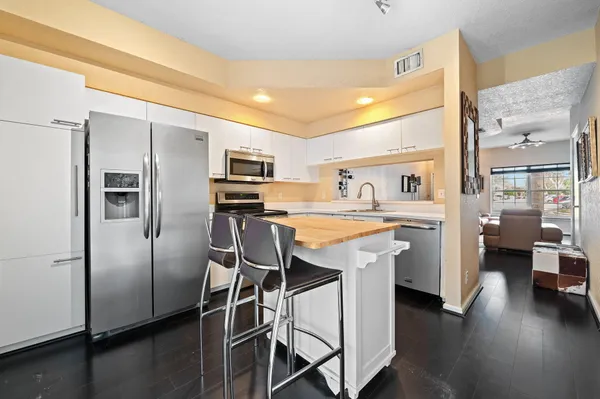 a kitchen with stainless steel appliances kitchen island granite countertop a refrigerator a sink a stove and white cabinets with wooden floor