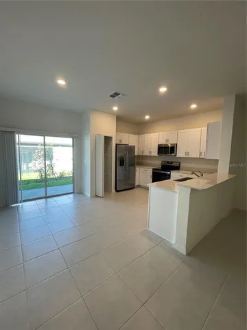 a large white kitchen with stainless steel appliances kitchen island granite countertop a refrigerator a stove a sink and a black cabinets with wooden floor