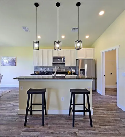 a kitchen with stainless steel appliances granite countertop a stove a sink a kitchen island with wooden floor and chairs