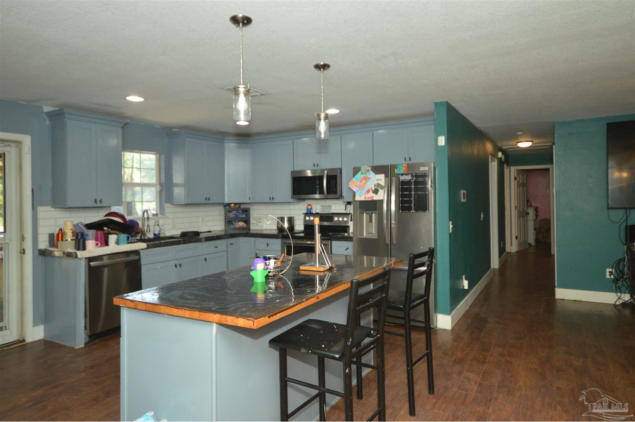 4163 Woodville Road Milton, FL 32583 - Photo 13 of 35 a kitchen with stainless steel appliances granite countertop a refrigerator a sink dishwasher a stove and a dining table with wooden floor
