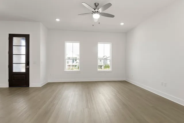 an empty room with wooden floor fan and windows
