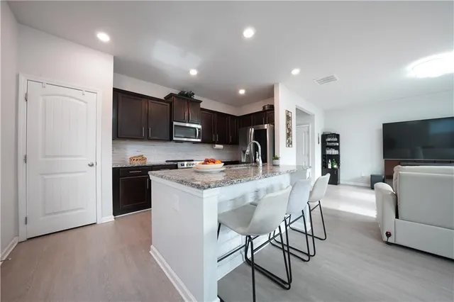 a kitchen with stainless steel appliances kitchen island granite countertop a refrigerator a stove a microwave oven a sink with a dining table and chairs