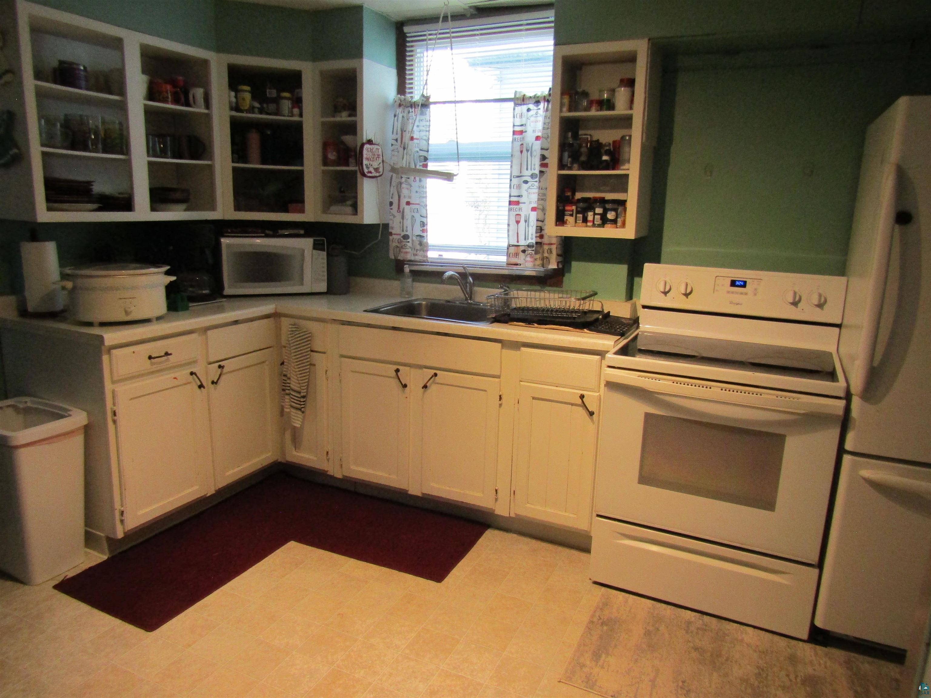 1115 Harrison Street Superior, WI 54880 - Photo 20 of 49 Kitchen featuring white cabinetry, a corner sink with window, vinyl flooring, and white appliances including a range and refrigerator