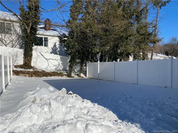 a view of white house next to a yard with large trees