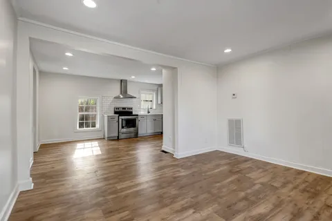an empty room with wooden floor and kitchen