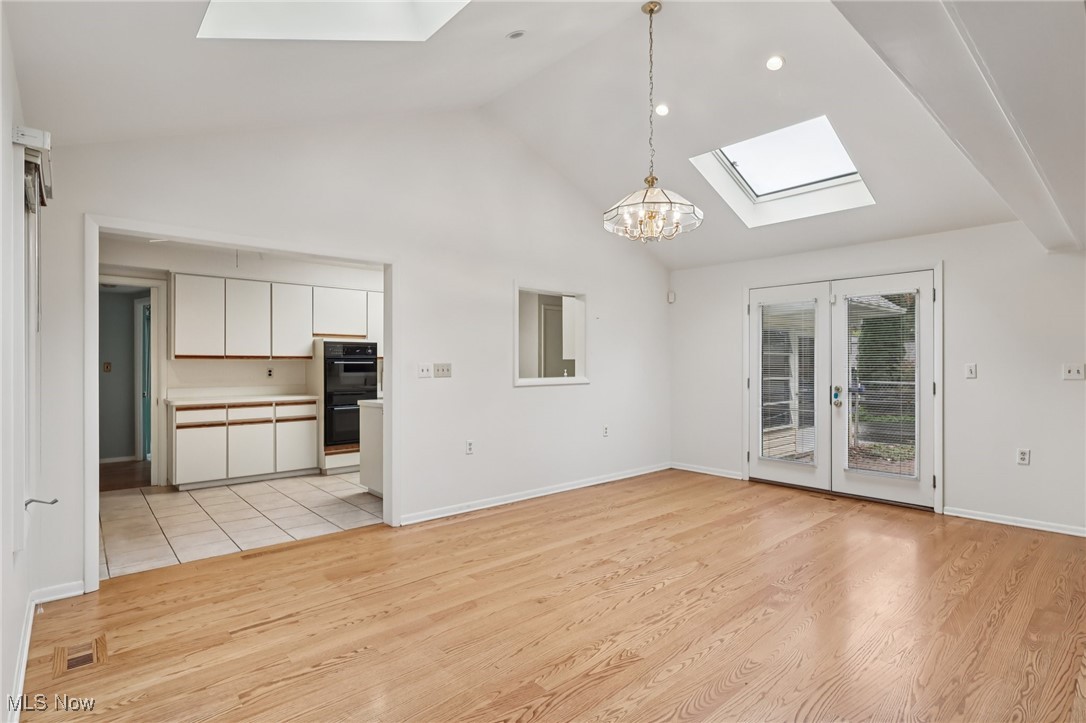 33300 South Woodland Road Cleveland, OH 44124 - Photo 20 of 50 Unfurnished living room with a skylight, light wood-style flooring, french doors, high vaulted ceiling, and a chandelier