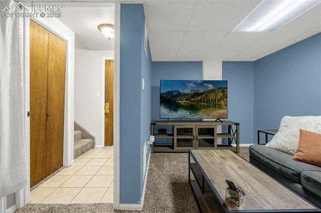 4990 Castledown Road Colorado Springs, CO 80917 - Photo 23 of 37 Living area with stairs, light tile patterned flooring, light carpet, baseboards, and a paneled ceiling