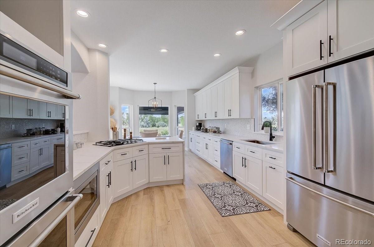 6063 South Eagle Street Centennial, CO 80016 - Photo 11 of 40 a large kitchen with stainless steel appliances kitchen island granite countertop a refrigerator oven a sink dishwasher and white cabinets with wooden floor