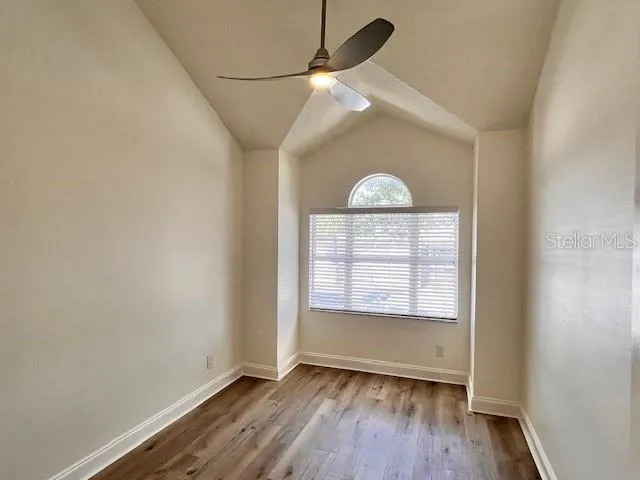 an empty room with wooden floor chandelier fan and windows
