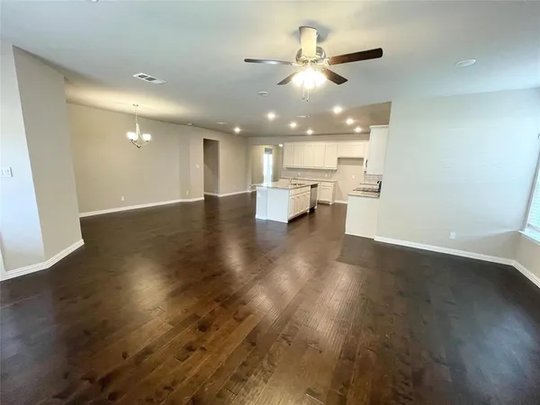 a view of an empty room and kitchen with wooden floor