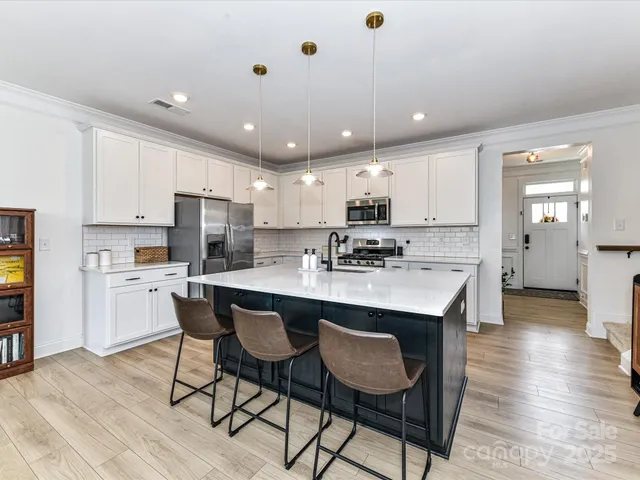 a kitchen with stainless steel appliances kitchen island granite countertop a table chairs refrigerator and microwave