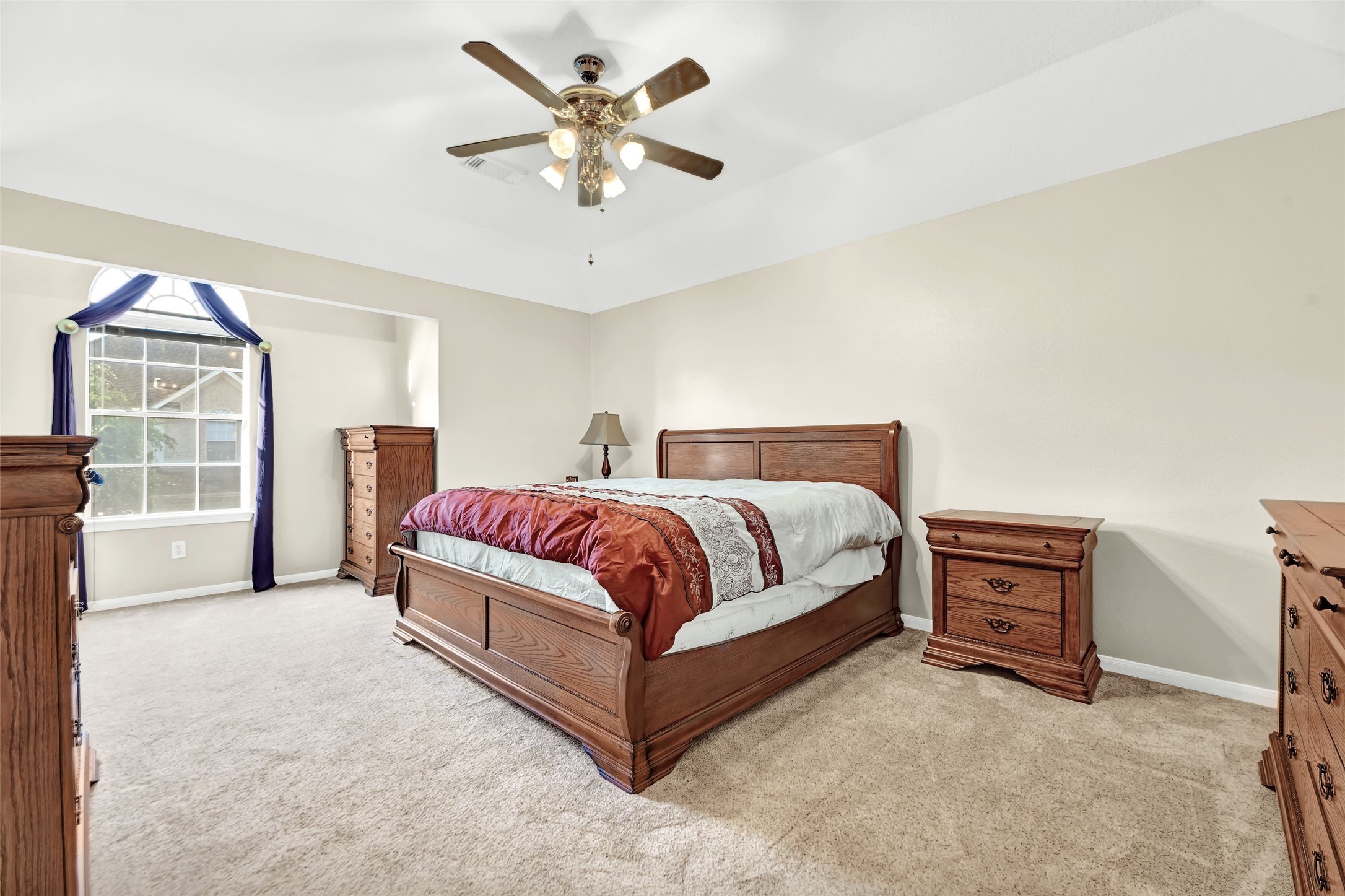14420 Walters Road, Unit 16 Houston, TX 77014 - Photo 20 of 27 This spacious bedroom features a cozy carpet, a ceiling fan, and ample natural light from a large window with elegant drapery. It includes classic wooden furniture, creating a warm and inviting atmosphere.