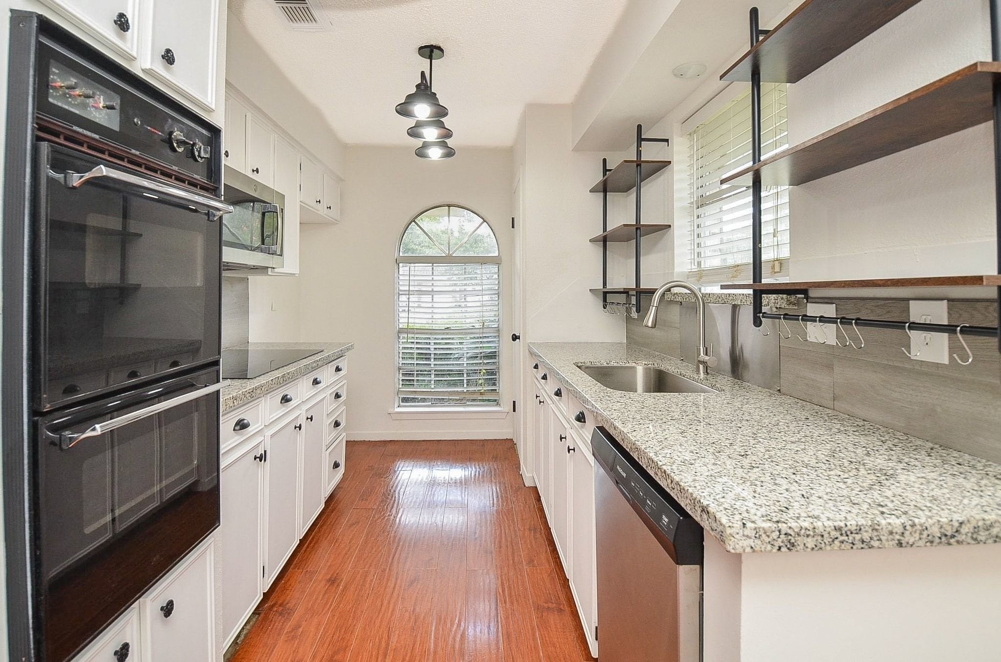 9014 Langfield Road Houston, TX 77040 - Photo 13 of 37 This functional efficiency kitchen blends modern upgrades with classic charm, featuring speckled granite countertops, white cabinetry with dark hardware, and rich wood-plank flooring.