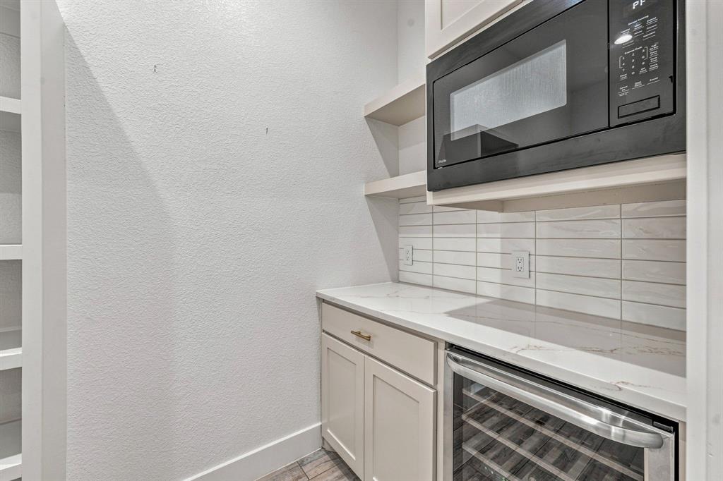 8140 Lavender Road Springtown, TX 76082 - Photo 13 of 40 Built-in microwave oven, under-counter beverage refrigerator, light-toned cabinetry with brass hardware, white horizontal tile backsplash, and light-toned countertops