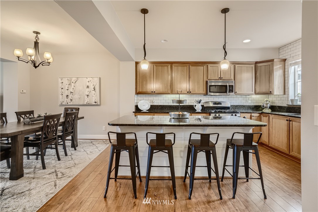 320 Chelan Place Northeast, Unit H3 Renton, WA 98059 - Photo 13 of 28 a kitchen with stainless steel appliances granite countertop a stove a refrigerator a kitchen island a dining table and chairs with wooden floor