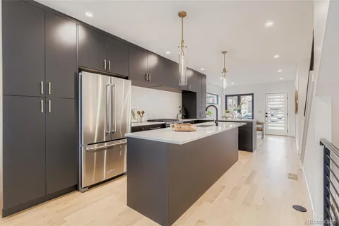 a large kitchen with stainless steel appliances kitchen island a stove a refrigerator a oven and a sink with wooden floor