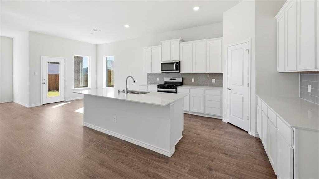 4163 Waldron Trail Forney, TX 75126 - Photo 29 of 30 Contemporary kitchen featuring an island with an undermount sink, white cabinetry, integrated stainless steel appliances, a tiled backsplash, and wood-finish flooring