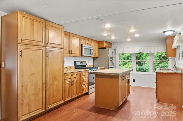 a kitchen with stainless steel appliances granite countertop a refrigerator a sink dishwasher a oven with white cabinets and wooden floor