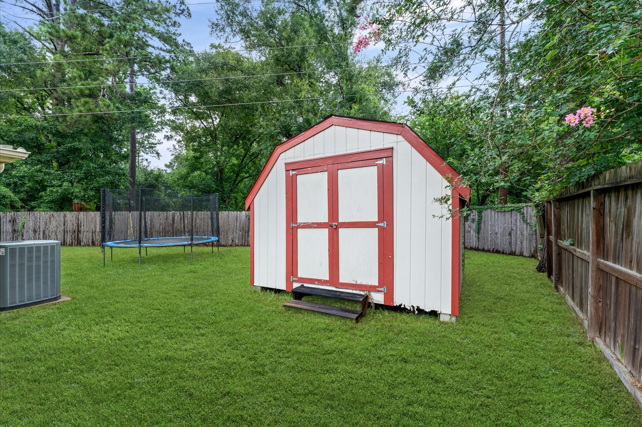 17618 Mill Springs Drive Spring, TX 77379 - Photo 25 of 26 Charming backyard featuring a spacious storage shed with a red trim, a large trampoline, and lush greenery, enclosed by a wooden fence for privacy.